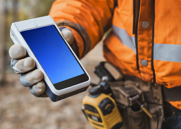 Person in orange safety jacket holding a card machine for trades and services.
